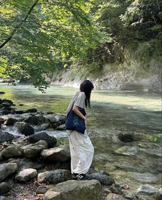 a woman standing on rocks in the middle of a river with water flowing behind her