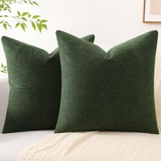 two green pillows sitting on top of a white couch next to a potted plant