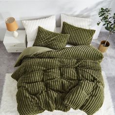 a bed with green comforter and pillows on top of white rugs in a bedroom