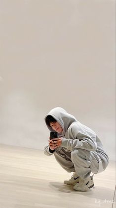 a person kneeling down and looking at a cell phone while wearing a hoodie on their head