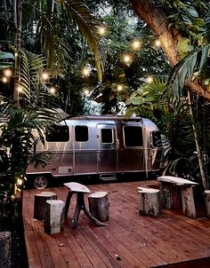 an rv is parked in the middle of some trees with lights strung from it's roof