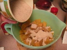 a person pouring sugar into a green bowl filled with cut up fruit and other ingredients