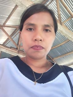 a woman wearing a cross necklace standing under a metal structure and looking at the camera