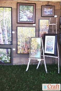 an outdoor art exhibit with paintings on the wall and trees in the backgroud