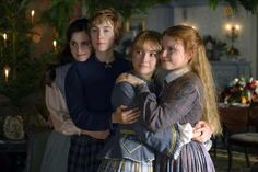 three girls hugging each other in a room with candles on the wall and christmas tree behind them