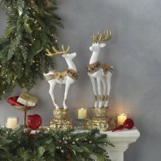 two white deer figurines sitting on top of a mantle next to a christmas tree