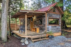 a small wooden cabin in the woods with a table and chairs on the front porch