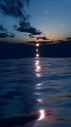 the moon is reflected in the water as it rises above the ocean at night time