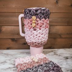 a crocheted coffee cup with a wooden handle on a marble countertop next to a wood wall