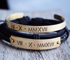 two bracelets with roman numerals on them sitting on top of a wooden table