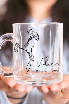 a person holding a clear glass mug with a flower on the side and name valerie maid of honor