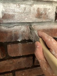 a hand holding a paint brush near a brick wall