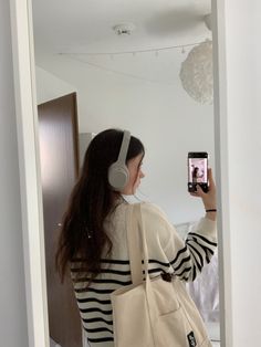 a woman wearing headphones is taking a selfie in the mirror with her cell phone