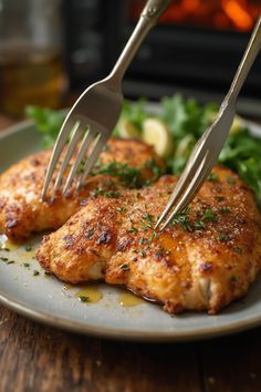 two pieces of chicken on a plate with a fork stuck in the meat and garnish