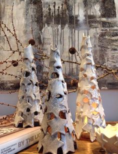 three ceramic trees sitting on top of a wooden table next to a book and painting