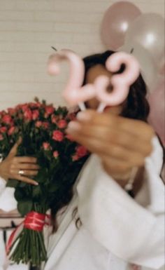 a woman holding flowers and balloons in front of her face with the number 20 on it