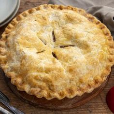 a pie sitting on top of a wooden cutting board next to a knife and fork