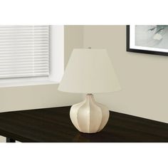 a white lamp sitting on top of a wooden table next to a framed photo and window