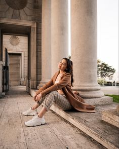 a woman is sitting on the ground in front of columns and looking up at the sky