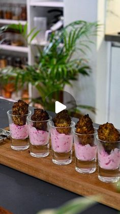 small cups filled with food sitting on top of a wooden table next to a plant