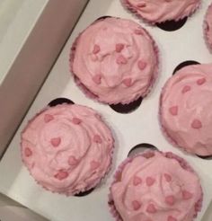 six cupcakes with pink frosting and hearts on them are in a box