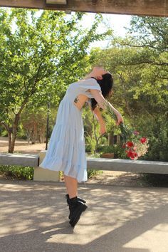 a woman in a blue dress is holding flowers and bending over to touch the ground