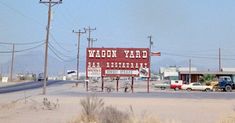 a red sign sitting on the side of a road in front of a gas station