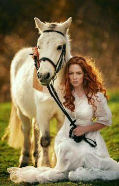 a woman in white dress sitting next to a horse