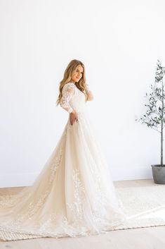 a woman in a white wedding dress standing on a rug next to a potted plant