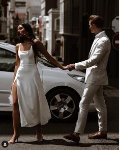 a woman in a white dress is holding the hand of a man in a suit