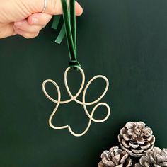 a hand holding a wire ornament next to pine cones