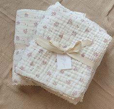 two baby blankets are wrapped in white fabric with pink flowers on them and a ribbon tied around the edges