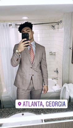 a man in a suit taking a selfie with his cell phone at the bathroom sink