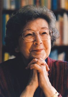 an older woman with glasses sitting in front of bookshelves