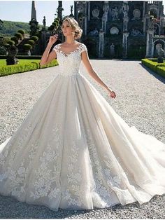 a woman in a wedding dress standing on a gravel road with an old castle in the background