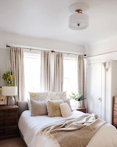 a white bed sitting in a bedroom next to a window covered in blankets and pillows