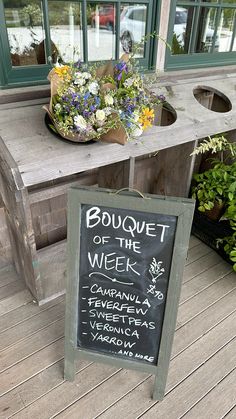 a chalkboard sign sitting on top of a wooden table next to potted plants