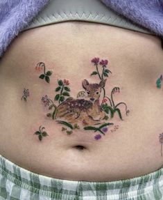 a woman's stomach with flowers and deer tattoo on her belly, which is surrounded by leaves