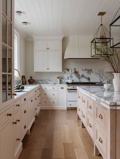 a kitchen with white cabinets and marble counter tops, along with wooden floors that match the ceiling