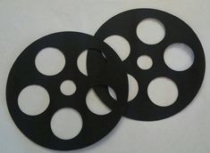 two black film reels sitting next to each other on a white surface with holes in the middle