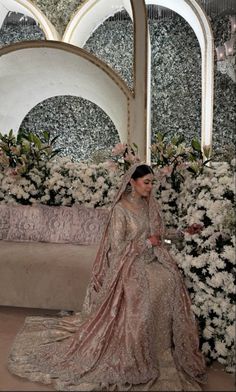 a woman in a wedding dress sitting on a couch with flowers around her neck and head