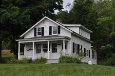 a white house sitting in the middle of a lush green field next to trees and bushes