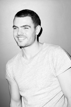 a black and white photo of a man in a t - shirt smiling at the camera