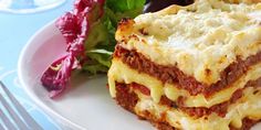 a white plate topped with lasagna next to a green leafy salad and fork