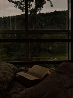 an open book sitting on top of a bed in front of a window next to a forest