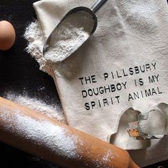 the flour is next to an egg and a rolling pin on a towel that says, the pillsbury doughboy is my spirit animal