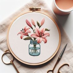 a glass jar with pink flowers in it next to scissors and a cup of coffee