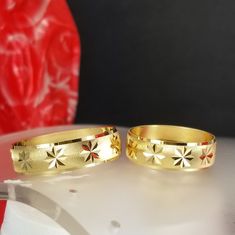 two gold rings sitting next to each other on a white surface with a red vase in the background