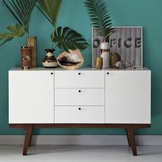 a sideboard with plants and pictures on it in front of a wall painted teal