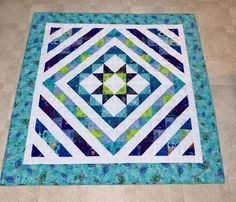 a blue, green and white quilt on the floor with an interesting design in it